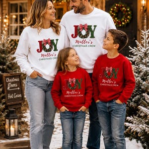 May include: White and red crewneck sweatshirts featuring the text JOY with a wreath replacing the letter O, a red and white checkered bow, and the custom text M&uuml;ller's CHRISTMAS CREW printed in a script and sans-serif font on the front.