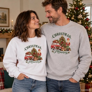 May include: A white sweatshirt and a grey sweatshirt, each featuring a graphic print of a red car, a decorated Christmas tree, and a nutcracker, with the text "CHRISTMAS Memories" in green and red script lettering centered on the chest.