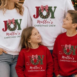 May include: Matching white and red crewneck sweatshirts featuring the word JOY with a green Christmas wreath as the letter O, topped with a red and white gingham bow. The text M&uuml;ller's CHRISTMAS CREW is printed below in a script and sans-serif font.