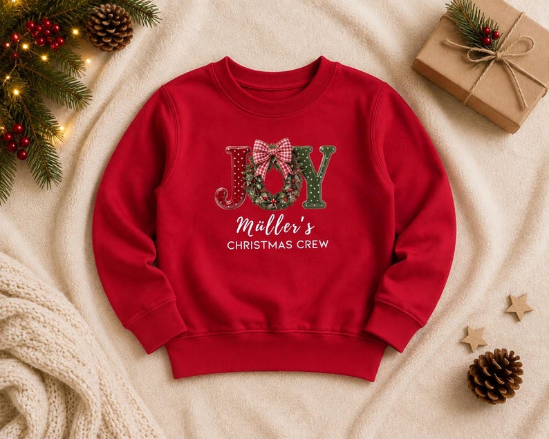 May include: A red long-sleeve sweatshirt featuring the word JOY with a green wreath replacing the letter O, topped with a red and white checkered bow. Below the graphic, the text reads M&uuml;ller's CHRISTMAS CREW in white lettering.
