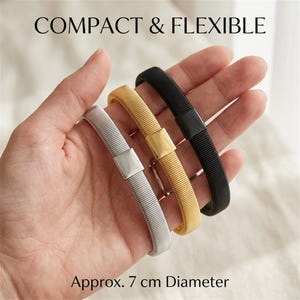 Puede incluir: Tres pulseras flexibles en tonos plata, oro y negro, cada una con una placa central rectangular lisa y un diseño de banda acanalada. El texto COMPACT & FLEXIBLE y Approx. 7 cm Diameter es visible. Diámetro de aproximadamente 7 cm.