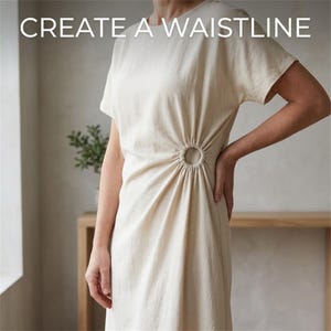 May include: A cream-colored short-sleeve dress featuring a circular ring detail at the waist that creates gathered fabric folds. The text "CREATE A WAISTLINE" is printed in white at the top of the image. The dress has a round neckline.