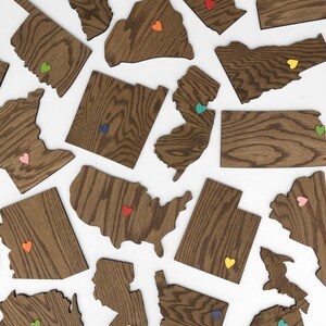 May include: A collection of wooden state outlines with colorful heart accents. Each state is a separate piece and has a unique wood grain pattern.