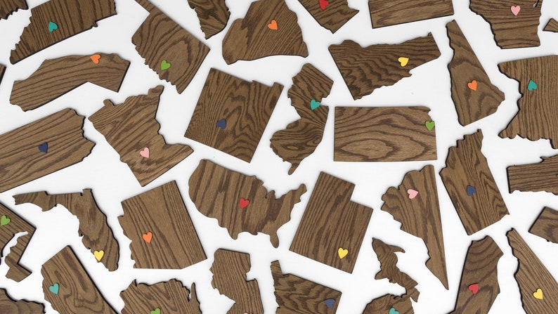May include: A collection of wooden state outlines with colorful heart accents. Each state is a separate piece and has a unique wood grain pattern.