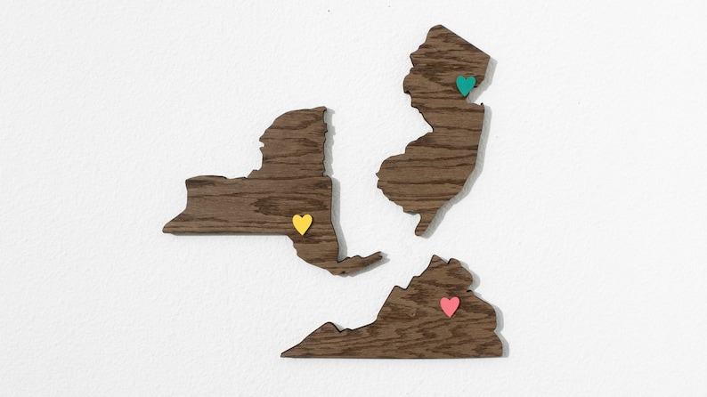 May include: Wooden cutout map of New York, New Jersey, and Virginia with colorful heart-shaped push pins. The New York pin is yellow, the New Jersey pin is teal, and the Virginia pin is pink.