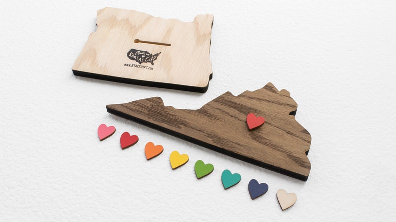 May include: Wooden cutout of the state of Virginia with a red heart placed on the state. A row of rainbow colored hearts are below the state. The back of the state cutout is made of dark wood. The text "Made in Kansas City" and "www.stategift.com" is printed on the back of the cutout.