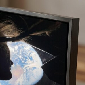 May include: Close-up of a dark-framed television displaying an image of Earth and a person's silhouette. The person's hair is visible. The TV frame is a dark, neutral color.