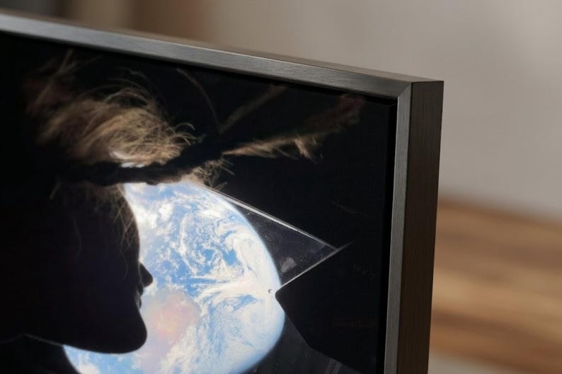 May include: Close-up of a dark-framed television displaying an image of Earth and a person's silhouette. The person's hair is visible. The TV frame is a dark, neutral color.