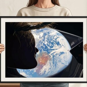May include: Framed art print featuring a silhouette of a person looking out a window at Earth from space. The artwork shows the Earth with blue oceans and white clouds. The frame is black.