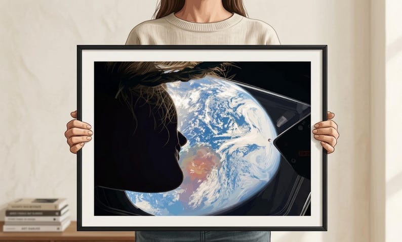 May include: Framed art print featuring a silhouette of a person looking out a window at Earth from space. The artwork shows the Earth with blue oceans and white clouds. The frame is black.