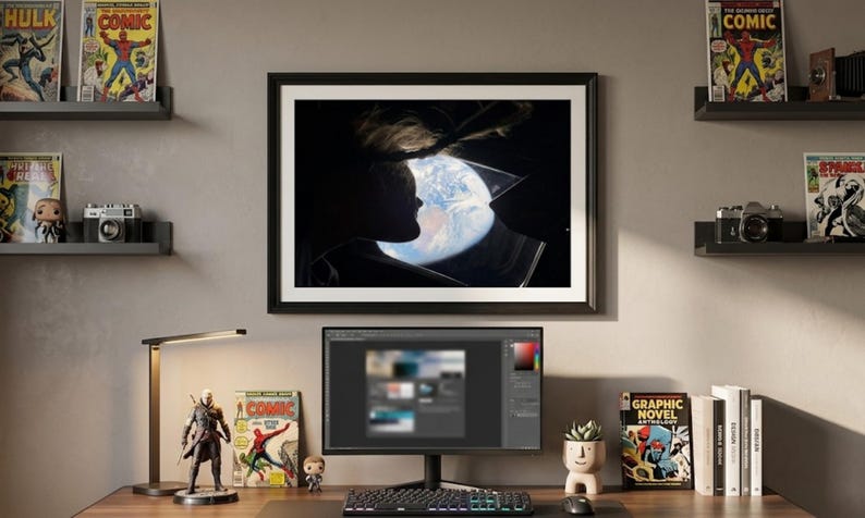 May include: A home office setup with a desk, computer, and framed artwork. Comic books and a desk lamp are visible. A figurine and a small potted plant add decorative touches. The computer screen displays a design program.