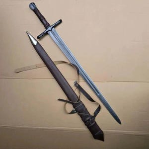 May include: A long, silver sword with a brown handle and crossguard, next to a brown leather sheath. The sheath has a gold-coloured tip and a leather strap. The sword's blade is long and sharp.