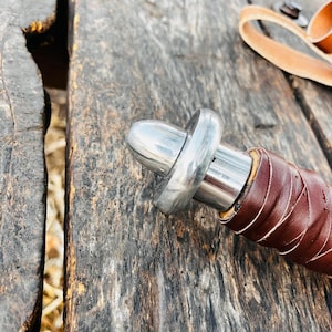 Top view of fantasy knife with leather sheath showing clean stitching and detailed finishing. The blade has a smooth reflective surface and a distinctive central groove design, while the sheath is crafted from quality leather for durability. A perfect display piece and thoughtful gift for husband or collectors who appreciate handcrafted items.