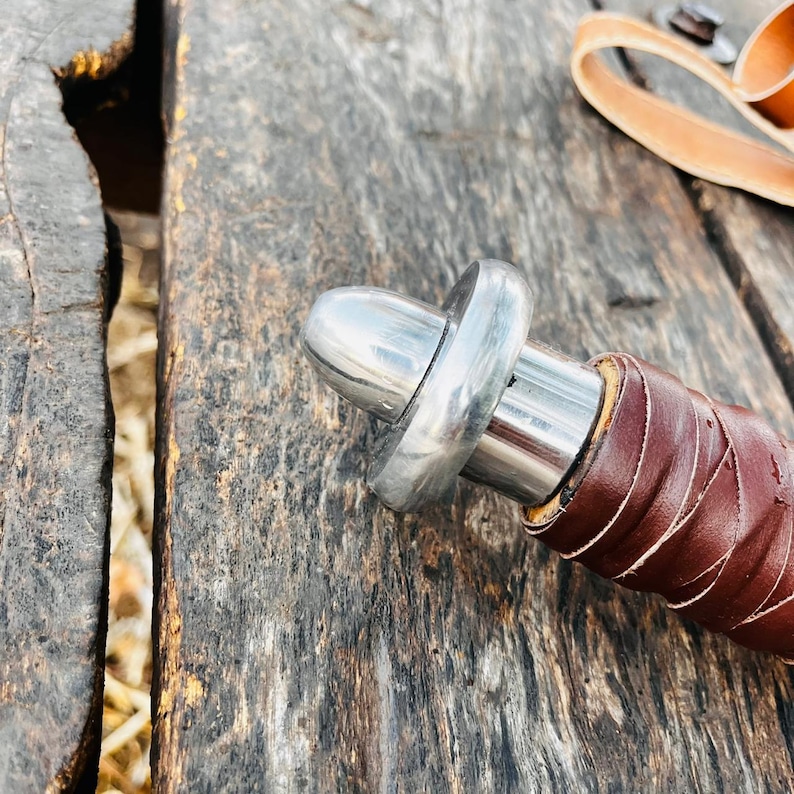 Top view of fantasy knife with leather sheath showing clean stitching and detailed finishing. The blade has a smooth reflective surface and a distinctive central groove design, while the sheath is crafted from quality leather for durability. A perfect display piece and thoughtful gift for husband or collectors who appreciate handcrafted items.