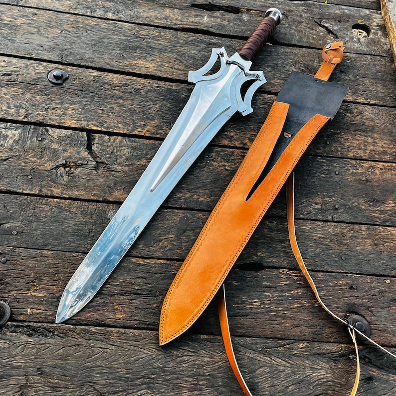 Custom handmade fantasy dagger style knife paired with a high quality leather sheath, captured in a clean top view to highlight overall craftsmanship. The long blade has a sleek reflective finish while the handle is wrapped in leather for comfort and control. This piece is perfect for collectors, display setups, or as a memorable gift for husband, boyfriend, or special occasions.