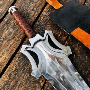 Handmade fantasy sword knife placed on a rustic wooden background highlighting its premium build and strong visual appeal. The long blade reflects light beautifully while the leather wrapped handle ensures a secure grip. Comes with a durable leather sheath, making it a great collector’s piece or a unique gift for husband, father, or boyfriend.