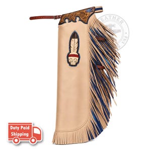 Peut inclure: Un chaps en cuir beige orné d'un motif de crâne et de plume, avec des gravures florales détaillées sur le haut et de longues franges alternant entre le beige et le bleu. Le vêtement comprend une sangle de ceinture en cuir marron avec boucle.