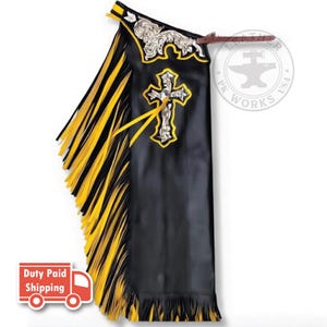 May include: Black leather chaps featuring long yellow and black fringe along the side. The upper section displays an ornate silver-toned floral embossed yoke and a prominent silver cross emblem with yellow trim. A brown leather strap is attached.