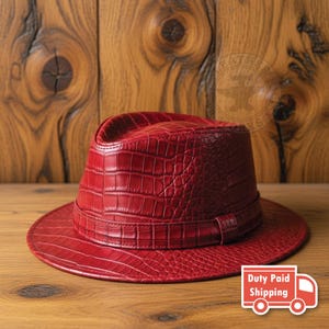 May include: A vibrant red fedora hat featuring a textured crocodile skin pattern across the crown and brim. The hat includes a matching red band encircling the base of the crown, showcasing a consistent embossed scale design throughout the entire piece.