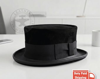 May include: A black top hat featuring a flat crown and a wide brim. The hat is adorned with a black grosgrain ribbon band that wraps around the base of the crown, featuring a small bow detail on the side. The texture appears smooth and matte.
