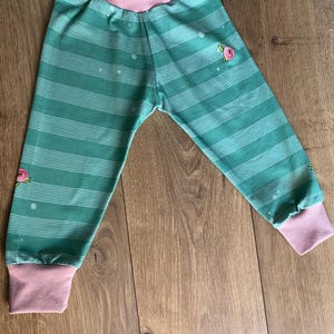 Puede incluir: Pantalones de bebé a rayas verdes y blancas, con puños y cintura rosas. Los pantalones presentan pequeñas aplicaciones de rosas rosas y lunares blancos. Fabricados en tejido suave para mayor comodidad.