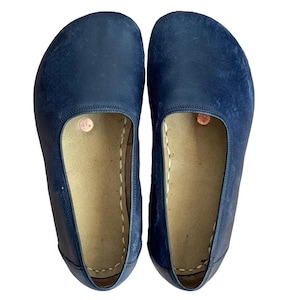 Puede incluir: Un par de zapatos sin cordones de cuero azul marino. Los zapatos tienen una puntera redondeada y una suela cosida. El interior es de color beige claro. Los zapatos están diseñados para la comodidad y el uso informal.