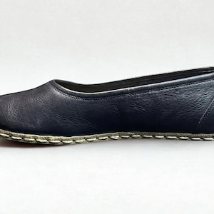 May include: A dark navy blue leather flat shoe with a rounded toe and a low-cut topline. The shoe features a visible, thick white whipstitch detail along the entire perimeter where the upper leather meets the sole, creating a distinct contrast.
