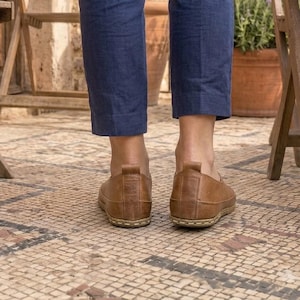 Puede incluir: Un par de zapatos marrones de cuero. Los zapatos se usan con pantalones azules. La imagen est&aacute; tomada desde un &aacute;ngulo bajo, mostrando los zapatos y la parte inferior de las piernas de la persona que los usa.