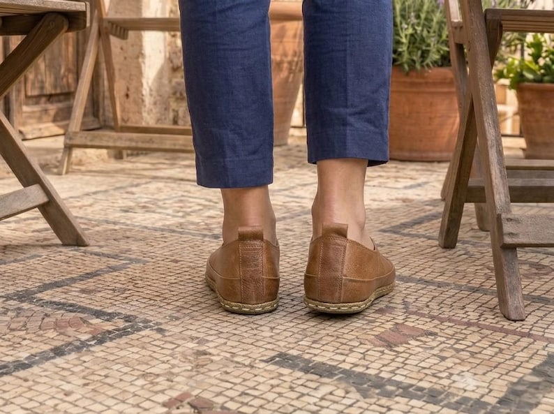 Puede incluir: Un par de zapatos marrones de cuero. Los zapatos se usan con pantalones azules. La imagen est&aacute; tomada desde un &aacute;ngulo bajo, mostrando los zapatos y la parte inferior de las piernas de la persona que los usa.