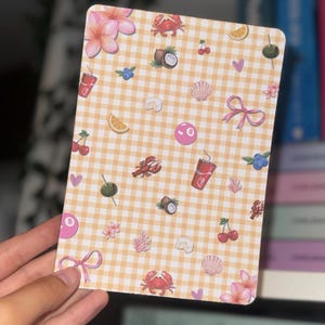 May include: A rectangular card with a yellow and white gingham pattern, decorated with illustrations. These include pink flowers, cherries, crabs, and a pink 8-ball. Other images include a seashell, a bow, and a drink.