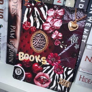 Op de afbeelding: Een rechthoekige print met een collage van rode en zwarte elementen, waaronder zebrastrepen, orchideeën, kersen, een achtbal, een gouden hartjesketting en een gouden lijst met de tekst Who needs therapy when books exist. De woorden BOOKS en XOXO zijn in goud weergegeven.