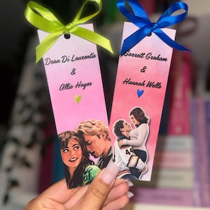 Op de afbeelding: Twee roze bladwijzers met illustraties van koppels, elk met een strik. Eén bladwijzer heeft een groene strik en de namen "Dean Di Laurentis & Allie Hayes". De andere heeft een blauwe strik en de namen "Garrett Graham & Hannah Wells".