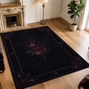 May include: A rectangular area rug featuring a deep black background with a central floral motif and matching corner accents. The design includes dark red and purple roses surrounded by small leaves and delicate blossoms, framed by a thin border.