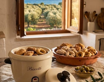May include: A cream-colored ceramic jar with a dark brown handle and lid, labeled with the word Biscotti in script. The jar contains several baked goods. A matching lid sits beside it, also featuring the word Biscotti and a dark brown knob.