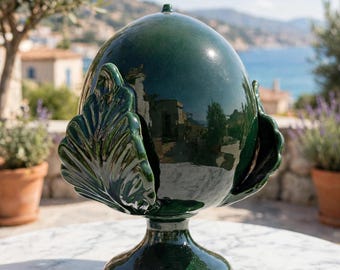 May include: A dark green ceramic pinecone ornament with a glossy finish, featuring a rounded top and stylized leaf-like scales. The decorative object is mounted on a circular pedestal base, showcasing a smooth, reflective surface throughout.