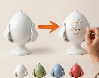 May include: A white ceramic pinecone-shaped ornament on a pedestal base with leaf-like side accents. One version features gold lettering that reads Giulia & Marco 2026. Additional smaller ornaments are shown in white, sage green, blue, and red.