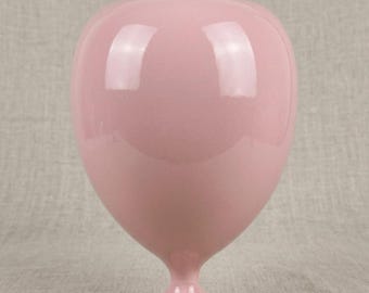 May include: A smooth, glossy, light pink vase with a rounded, bulbous body that tapers down to a narrow neck and a small, circular pedestal base. The surface of the vase reflects light, highlighting its curved, symmetrical, and solid form.