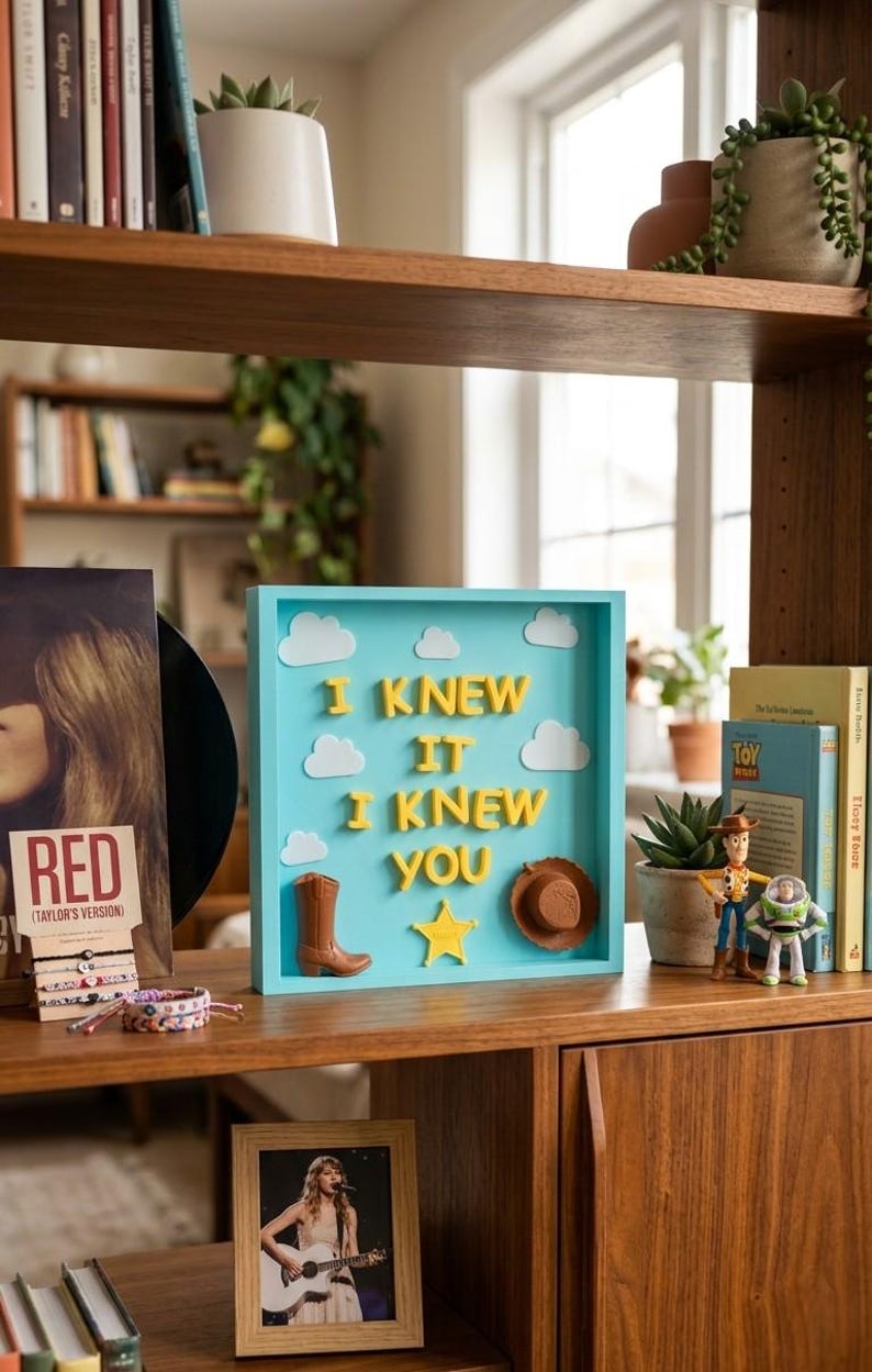 Pu&ograve; includere: Una scatola quadrata azzurra con il testo in rilievo giallo I KNEW IT I KNEW YOU. L'espositore include ritagli di nuvole bianche, uno stivale da cowboy marrone, una stella gialla e un cappello da cowboy marrone fissati sullo sfondo azzurro.