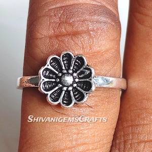 Könnte beinhalten: Ein silberner Ring mit einem blütenförmigen Design, das detaillierte Blütenblätter und eine zentrale Perle aufweist. Der Ring wird an einem Finger getragen, mit dem Markennamen "SHIVANIGEMSCRAFTS".