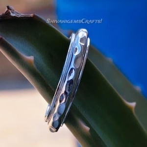 Könnte beinhalten: Ein silberner Ring mit gehämmertem Muster liegt auf einem grünen Aloe Vera Blatt. Der Ring hat eine Reihe kleiner, gleichmäßig verteilter Vertiefungen. Der Hintergrund ist ein verschwommenes Blau, mit dem Text "SHIVANIGEMSCRAFTS!" sichtbar.