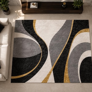 May include: A large area rug with an abstract design in shades of black, gray, and cream, accented with gold lines. The rug is rectangular and covers a significant portion of the floor. The room also features a white sofa, armchairs, and a dark wood cabinet.