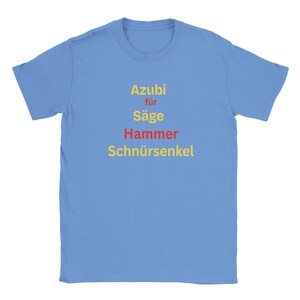 May include: A light blue t-shirt featuring the German words "Azubi für Säge Hammer Schnürsenkel" in yellow and red. The text is centered on the front of the shirt.