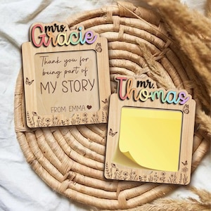 Può includere: Due cornici in legno con testo colorato e disegni floreali. Una cornice dice "Mrs. Gracie" e "Thank you for being part of MY STORY" con "FROM: EMMA". L'altra dice "Mr. Thomas" e contiene un post-it giallo. Farfalle e fiori decorano le cornici.