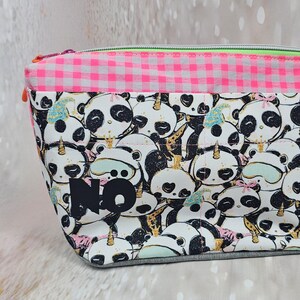 Könnte beinhalten: Eine rechteckige Kosmetiktasche mit Reißverschluss. Die Tasche hat ein sich wiederholendes Muster von Pandabären mit Einhorn-Hörnern und Schlafmasken. Der obere Teil ist rosa und weißes Vichy, und das Wort "NO" ist auf der Vorderseite aufgedruckt.