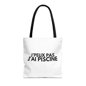 Peut inclure: Sac fourre-tout blanc avec des anses noires. Le sac affiche le texte "J'PEUX PAS J'AI PISCINE" en noir, centré sur le devant. Le sac est fait d'une matière souple et convient au transport de divers articles.