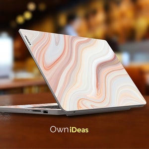 May include: A white laptop with a marble-like design on the lid. The laptop is closed and the Lenovo logo is visible on the lid. The laptop is sitting on a wooden table.