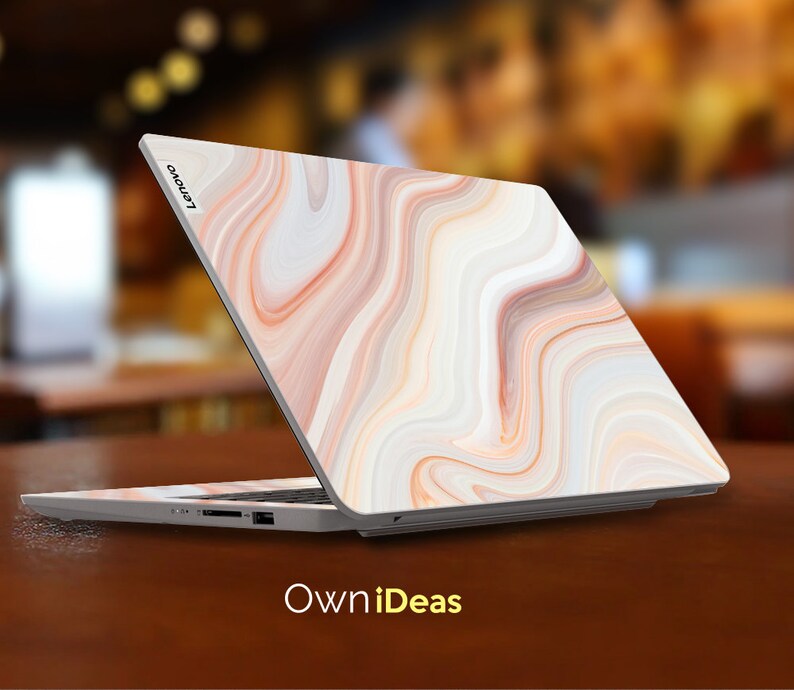 May include: A white laptop with a marble-like design on the lid. The laptop is closed and the Lenovo logo is visible on the lid. The laptop is sitting on a wooden table.