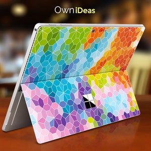 Puede incluir: Un portátil plateado con un patrón geométrico colorido que cubre su superficie. El patrón presenta una variedad de colores, incluyendo azul, verde, naranja, rosa y morado. El portátil está cerrado y la pantalla está orientada hacia el espectador. El texto "OwnIdeas" está impreso en la parte superior del portátil.