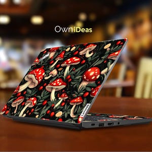 May include: A Lenovo laptop with a custom skin featuring a pattern of red mushrooms with white spots and green foliage on a black background. The laptop is open on a brown surface, with the text "OwniDeas" visible.