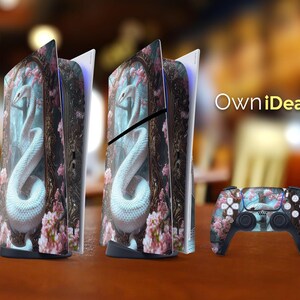 以下が含まれることがあります： 白い蛇と花のデザインが施された、白と青のPlaystation 5コンソールスキン2枚。スキンは木製のテーブルの上に置かれています。背景には「OwnIdeas」というテキストが表示されています。白と青のPlaystation 5コントローラーもテーブルの上に置かれています。